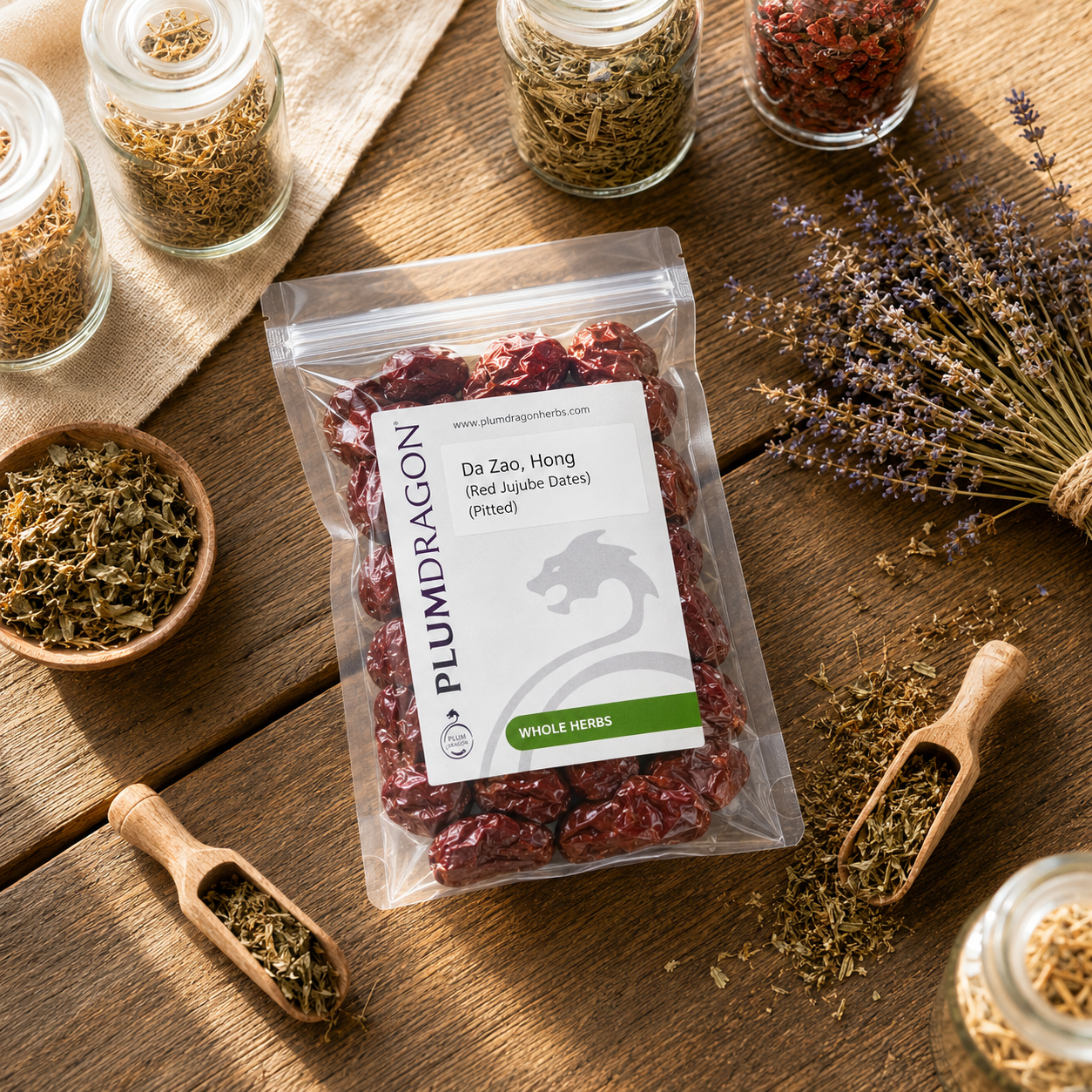 Packaged Da Zao Hong (Red Jujube Dates) with a Plum Dragon Whole Herbs label on a wooden surface with various herbs and a wooden scoop.
